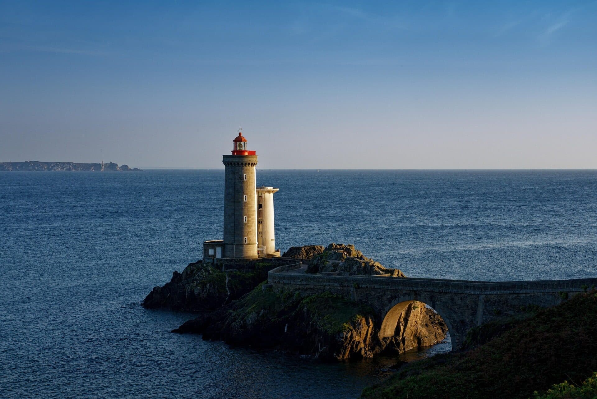 Farol sobre um rochedo à beira-mar, iluminado pelo sol do fim de tarde